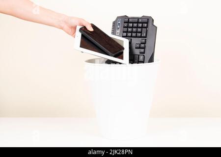 Weibliche Hand bringt gebrauchte digitale Tablet-Computer und Handys in Recycling-Papierkorb voll von alten elektronischen Geräten. Geplante Obsoleszenz, E-Waste Stockfoto