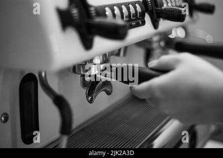 Der Barista hält einen Halter und macht Kaffee mit einer Doppelkessel-Kaffeemaschine Stockfoto