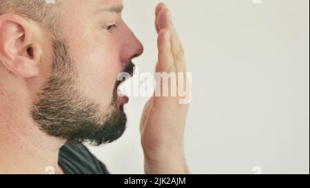 Schlechter Atem. Das Konzept der Mundgeruch. Ein junger Mann prüft seinen Atem mit der Hand Stockfoto