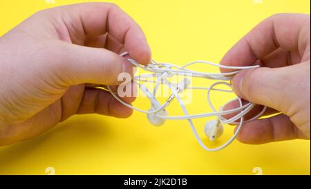 Die Hände des Mannes versuchen, die verworrenen Kopfhörer auf einem gelben Hintergrund zu entwirren. Schließen Stockfoto