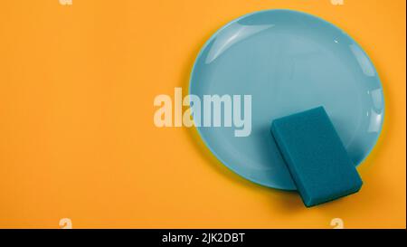 Reinigungsschwamm auf einer grünen Platte auf einem orangefarbenen Hintergrund Stockfoto