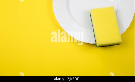 Spülkonzept. Teller mit Schwamm auf gelbem pastellfarbenem Hintergrund. Draufsicht Stockfoto