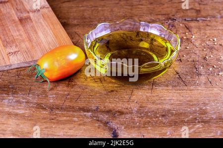 Natives Olivenöl extra in Glas und Tomate auf rustikalem Holztisch Stockfoto