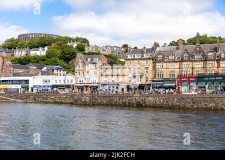 Oban Stadtzentrum an sonnigen Sommertagen, Geschäfte und Touristen in der Stadt mit Blick auf McCaig's Turm, Oban, Argyll, Schottland, Großbritannien Stockfoto