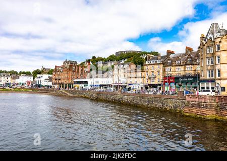 Oban Stadtzentrum an sonnigen Sommertagen, Geschäfte und Touristen in der Stadt mit Blick auf McCaig's Turm, Oban, Argyll, Schottland, Großbritannien Stockfoto