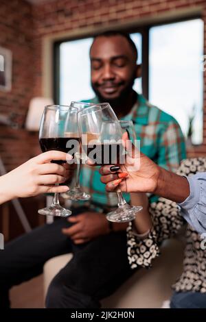 Fröhliche, multirassische Gruppe von besten Freunden, die Weingläser toasten, während sie zu Hause eine Weinparty genießen. Fröhliches Lächeln verschiedene Menschen klirren Gläser während der Feier Geburtstagsfeier. Stockfoto