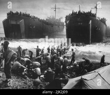 Zwei von der Küstenwache bemannte LST öffnen ihre großen Kiefer in der Brandung, die am Strand von Leyte Island gewaschen wird, während Soldaten sich abstreifen und Sandsäcke an den Rampen bauen, um die Entladeoperationen zu beschleunigen. Stockfoto