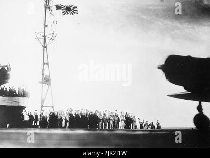 Ein erfasstes japanisches Foto, das vor dem Angriff auf Pearl Harbor an Bord eines japanischen Transporters aufgenommen wurde, 7. Dezember 1941. Es zeigt die Männer, die ihre Arme zum Gruß erheben, mit der Silhouette eines Flugzeugs und der Flagge der aufgehenden Sonne. Der Propeller im Flugzeug dreht sich, so dass dieses Bild möglicherweise aufgenommen wurde, als die Flugzeuge in ihrer berühmten und berüchtigten Mission abreisten. Stockfoto