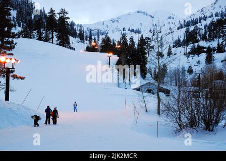 Skifahrer und Snowboards beenden ihren Lauf auf den Schneehängen, wenn die Sonne im Olympic Valley, Kalifornien, untergeht Stockfoto