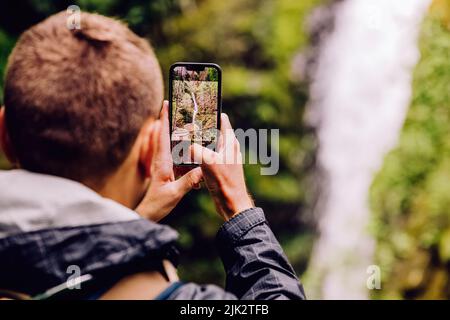 Mann, der mit seinem Telefon einen malerischen Wasserfall fotografiert, Nahaufnahme Stockfoto