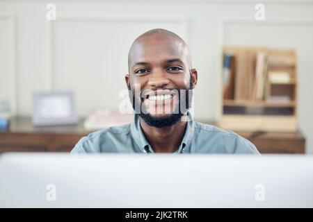 Täglich auf mein Ziel zuarbeiten. Ein hübscher junger Geschäftsmann, der allein in seinem Büro sitzt und seinen Computer benutzt. Stockfoto