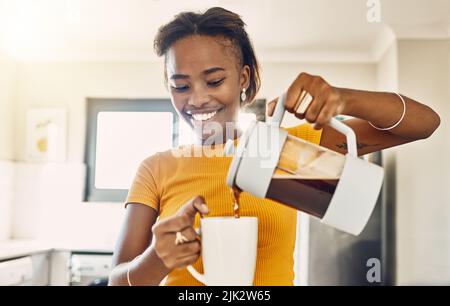 Schöne, glückliche und entspannte Frau, die Kaffee macht und heiße Getränke in die Tasse gießt, um morgens die Hausküche zu genießen. Junge lächelnde Dame bereitet oder vor Stockfoto