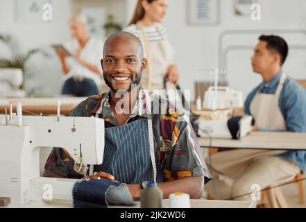 Modedesigner, junger Mann und kreativ in einem Workshop Nähen Kleidung. Porträt eines glücklichen, lächelnden und fröhlichen Fabrikarbeiters an einer Nähmaschine Stockfoto
