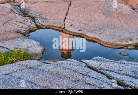 Peggys Cove Lighthouse spiegelte sich in einem Wasserbecken wider, das bei Sonnenuntergang in einer Depression in den Felsen gefangen war. Stockfoto
