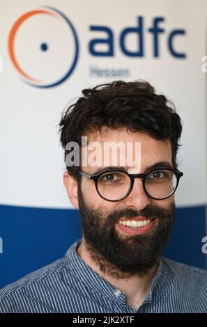 27. Juli 2022, Hessen, Frankfurt/Main: Sofrony Riedmann, die neue Geschäftsführerin des ADFC Hessen, steht in seinem Büro vor einem Display mit dem ADFC-Logo. Im Kampf um eine Verkehrskehrtwende will der ADFC auch ungewöhnliche Allianzen schmieden, um den Druck auf die Politik zu erhöhen. Riedmann leitet den Verein seit dem 1. Juli 2022 als Geschäftsführer. (An dpa 'Neuer ADFC-Geschäftsführer gibt Radwegen in Hessen eine schlechte Note') Foto: Arne Dedert/dpa Stockfoto