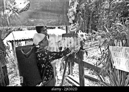 Dorf Uluk Palin, Putusibau Utara, Kapuas Hulu, West Kalimantan, Indonesien. März 2007. Traditioneller Häuptling der Dayak Tamambaloh Longhouse Gemeinschaft, der Blumen am Grab des ehemaligen Häuptlings zusammen mit seiner Frau, der ältesten Tochter des verstorbenen Häuptlings, arrangiert. Ein Besuch auf dem Friedhof ist Teil einer Reihe traditioneller Veranstaltungen zu Ehren des ehemaligen traditionellen Häuptlings, der einige Wochen zuvor verstorben ist. - Fotografiert auf Schwarzweißfilm, gescannt, digitalisiert. Stockfoto