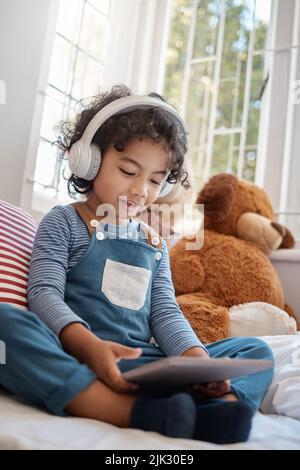 Sorgen Sie dafür, dass Freundlichkeit und sanfte Sprache Ihre Natur dominiert. Ein entzückender Junge mit einem digitalen Tablet und Kopfhörer in seinem Schlafzimmer zu Hause. Stockfoto