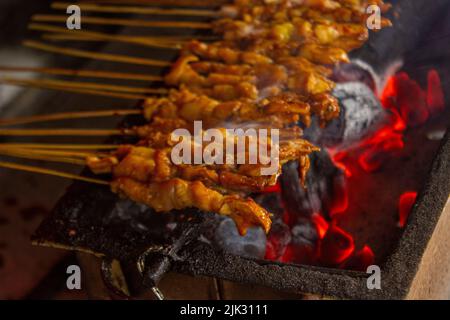 Sate ayam oder Hähnchen-Satay, oder Huhn oder Fleisch-Satay mit Holzkohle Zutat auf rotem Feuer Grill von Menschen. Traditionelle Satay aus, Indonesien Stockfoto