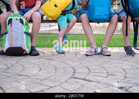 Beschnittenes Bild von Schulkindern, die mit ihren Rucksäcken auf einer Bank sitzen. Stockfoto