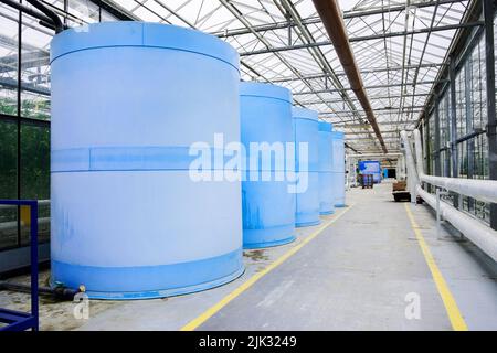 Wasserpumpe mit Elektromotor am Gewächshaus. Interieur und Ausstattung mit Rohrleitungen und Wasserbehälter in modernem Gewächshaus. Moderne Gewächshaus-Ausrüstung für Stockfoto