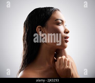 Sie ist Perfektion. Eine attraktive junge Frau, die nachdenklich aussieht, während sie im Studio vor einem grauen Hintergrund posiert. Stockfoto