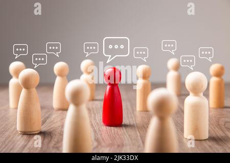 Rote Anführer-Figur spricht mit einer vielfältigen Gruppe von Holzfiguren mit Sprechblasen Stockfoto