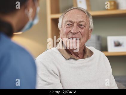 Ein glücklicher und gepflegter Patient. Ein älterer Mann, der zu Hause eine Untersuchung mit einer nicht erkennbaren Krankenschwester macht. Stockfoto