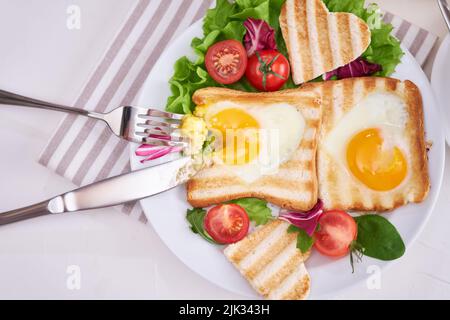 Herzförmige gebratene Eier auf Toastbrot auf hellgrauem Hintergrund Stockfoto