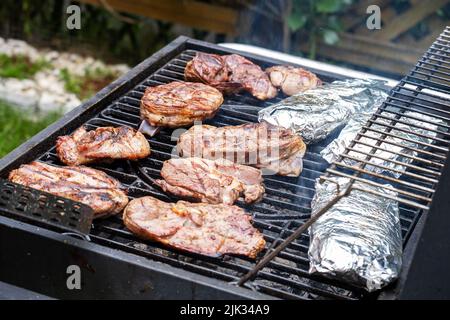 Frisches Fleisch und Fisch in Folie werden auf einem Grillrost ausgelegt. Stockfoto