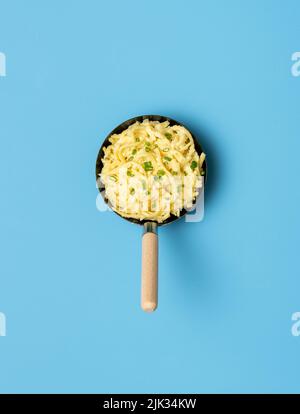 Oben gesehen spätzle in einer Pfanne auf einem blauen Tisch. Deutsches Gericht mit Nudeln, Käse und Schnittlauch. Stockfoto