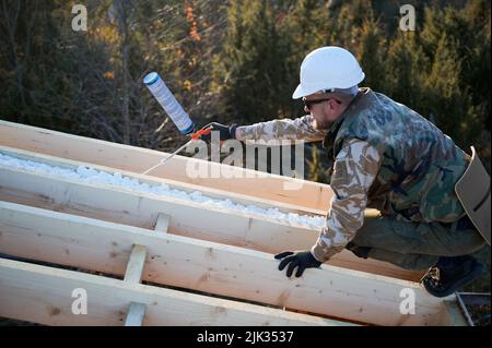 Männlicher Baumeister macht Wärmedämmung auf dem Dach des Holzrahmenhauses. Mann Arbeiter sprühen Polyurethan-Schaum auf dem Dach der zukünftigen Hütte. Bau- und Isolierkonzept. Stockfoto