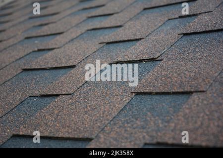 Kupfer, braun architektonischen, dimensionalen Asphalt Dachschindeln Hintergrund. Nahaufnahme eines Daches, das mit braunen Asphaltschindeln bedeckt ist. Stockfoto