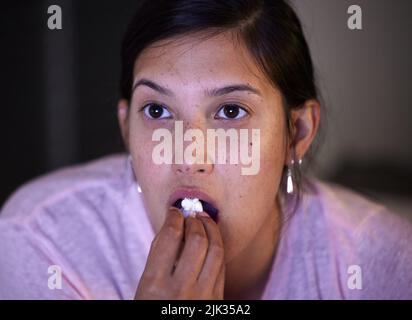 Die Handlung verdickt sich. Eine junge Frau, die Popcorn isst, während sie zu Hause fernsehen. Stockfoto