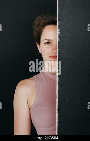 Eine schöne Brünette gucken hinter einem schwarzen Bildschirm hervor. Porträt eines jungen Mädchens in rosa Kleidung. Stockfoto