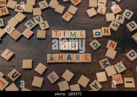 ZEIT ZUM TEILEN. Holzwort Spiel Konzept. Quadratische bunte Buchstaben auf einem dunklen Holztisch. Beziehungskonzept. Hochwertige Fotos Stockfoto