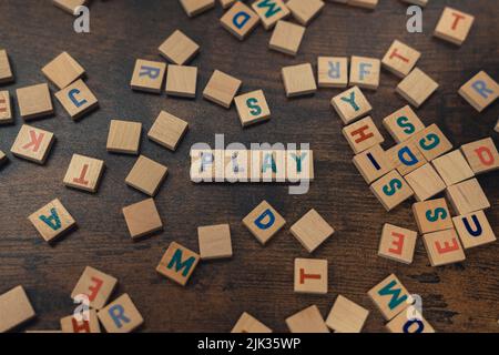 Verstreutes Wortspiel aus Holz. Bunte quadratische Buchstaben auf einem dunklen Holztisch schaffen das WORTSPIEL. Freizeitangebot. Hochwertige Fotos Stockfoto