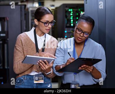 Zwei attraktive junge Computerprogrammiererinnen arbeiten in einem Serverraum zusammen. Stockfoto