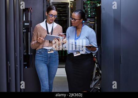 Hier gibt es keine Verbindungsprobleme. Zwei attraktive junge Computerprogrammiererinnen arbeiten in einem Serverraum zusammen. Stockfoto