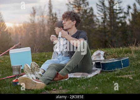 Junge männliche und weibliche Touristen Freunde sitzen auf Gras und trinken Tee oder Kaffee. Stockfoto