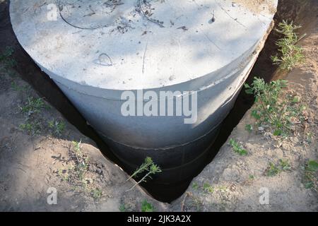 Installation eines Klärgruben aus Betonringen. Betonabwasserkanalöffnung, Schachtringe werden in ein quadratisches Loch eingebaut. Stockfoto