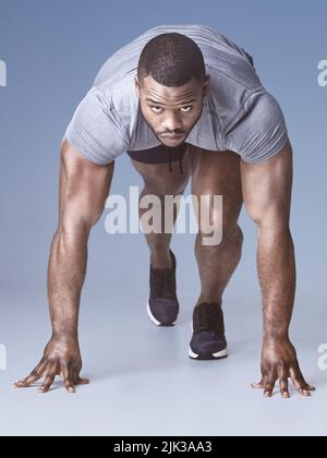 Sei derjenige, der sich dafür eingesetzt hat. Die ganze Aufnahme eines hübschen jungen Mannes, der sich in einer Startposition im Studio kauerte. Stockfoto