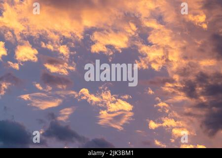 Purpurner Himmel mit flauschigen orangen und gelben Wolken bei Sonnenuntergang. Stockfoto