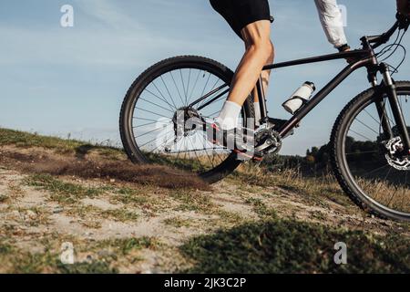Cropped unkenntlich professioneller Radsportler steigt mit seinem Mountainbike eine Steigung hinab, der Sportler fährt mit dem Fahrrad bergab Stockfoto