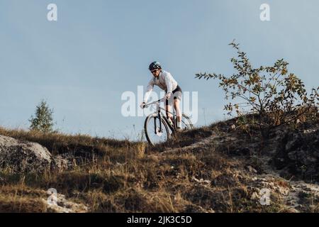 Ausgerüsteter Profi-Radler fährt mit seinem Mountainbike eine Piste hinunter, der Sportler fährt mit dem Fahrrad vom Berg herunter Stockfoto