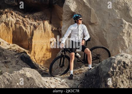 Der professionelle Radsportler lehnt sich an sein Fahrrad und der Erwachsene Mann genießt die Ruhe während seiner Fahrradtour Stockfoto