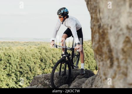 Ausgerüsteter Profi-Radler mit Mountainbike auf dem Trail im felsigen Gelände, Erwachsener, der seinen extremen Hobby mit Fahrrad auf genießt Stockfoto