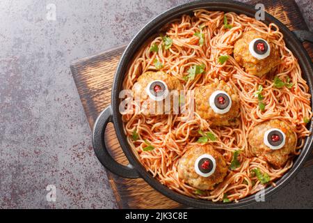 Halloween-Dinner mit Fleischbällchen mit Monsteraugen und Pasta mit Tomatensauce in einer Pfanne auf dem Tisch aus nächster Nähe. Horizontale Draufsicht von oben Stockfoto