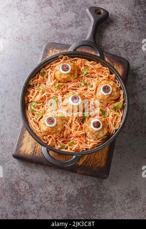 Spaghetti mit Tomatensauce und Fleischbällchen mit lustigen Augen auf dem Tisch aus der Nähe. Lustige Dekorationen. Halloween-Essen. Vertikale Draufsicht von oben Stockfoto