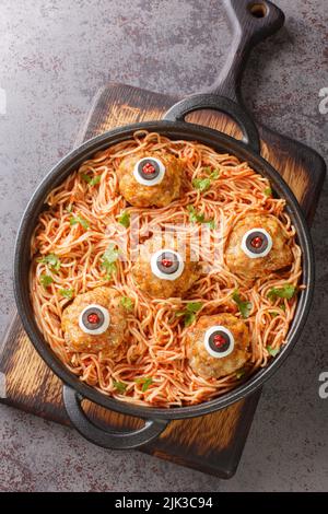 Pasta dekoriert mit Fleischbällchen Augen Nahaufnahme in den Teller auf dem Tisch Menü an Halloween. Vertikale Draufsicht von oben Stockfoto