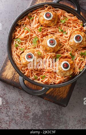 Gruselig leckeres Halloween Essen aus Fleischbällchen mit Monsteraugen und Spaghetti mit Tomatensauce in einer Pfanne auf dem Tisch aus der Nähe. Vertikale Draufsicht von oben Stockfoto